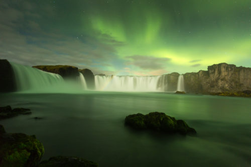 The beautiful green aurora borealis display over the famous Goðafoss waterfall in northern Iceland.