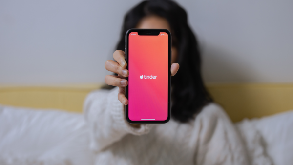 Vrouw houdt een telefoon vast voor haar gezicht met daarop de datings app Tinder