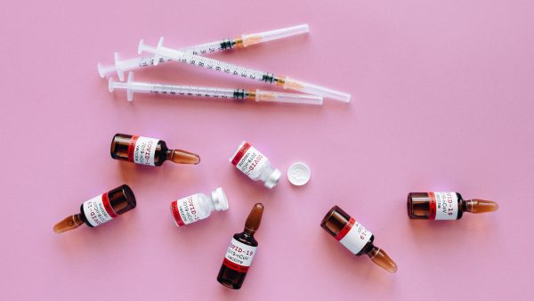 Drie covid-19 vaccins gestrooid op een roze achtergrond, naast buisjes en medische voorwerpen