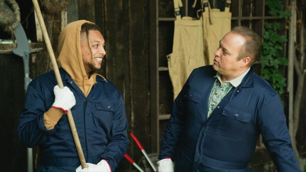 Ronnie en Frans Bauer op een boerderij met een bezem kijken elkaar aan