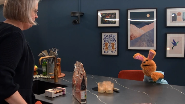 Saskia komt het huis binnen en wordt begroet door een handpop: