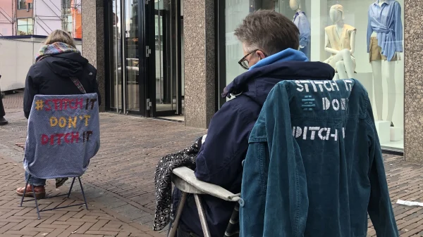 Kitty verstelt kleding op een klapstoel in de winkelstraat: 'Koop niet méér, maar repareer'