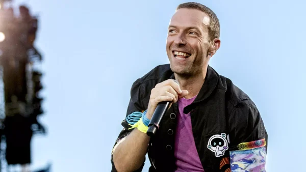 Chris Martin van Coldplay houdt microfoon vast en lacht tijdens een optreden