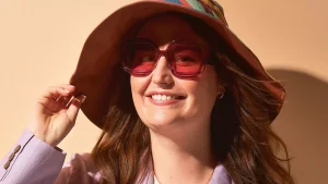 Shauni met een zonnebril en een hoed op voor een oranje achtergrond