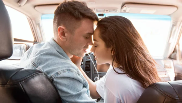 Man en vrouw geven zoen tijdens autorit, hij zit achter het stuur in de auto