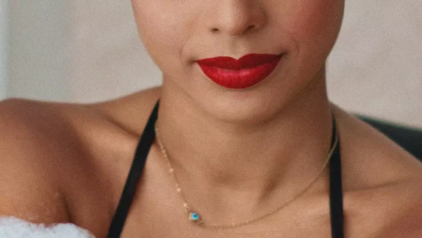 Close-up foto van een vrouw met rode lippenstift en gouden sieraden om haar nek