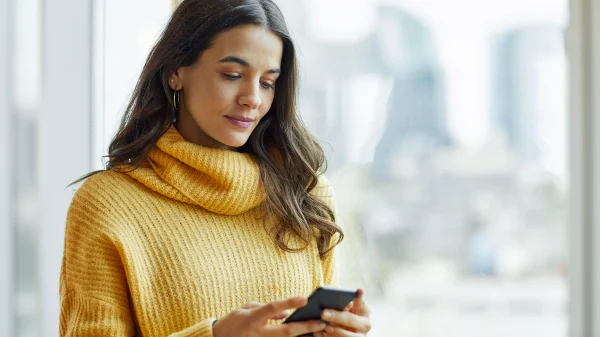 Vrouw met gele trui aan kijkt naar haar telefoon