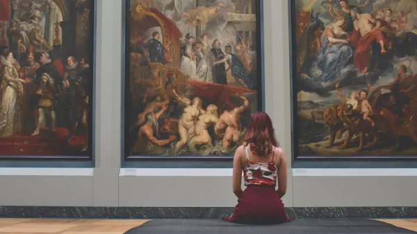 Vrouw zit voor drie schilderijen in een museum