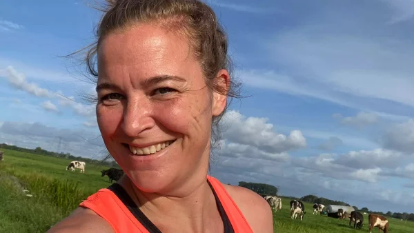 Marnel draagt hardloopkleding terwijl ze langs een weiland loopt en lacht naar de camera