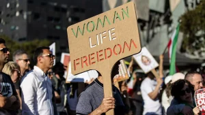 Protest voor Mahsa Amini | Een protestant houdt een bord omhoog met daarop de leus 'woman, life, freedom'
