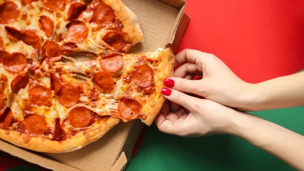 Iemand haalt een stuk pizza uit een pizzadoos