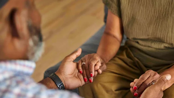 Een man en vrouw zitten tegenover elkaar en houden elkaars handen vast | Jada vertelt over de laatste weken van haar vader