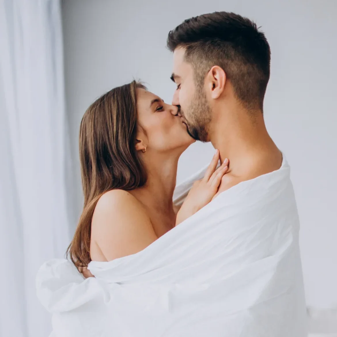 Man en vrouw zijn gewikkeld in een witte deken en geven een zoen op hun huwelijksnacht