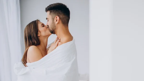 Man en vrouw zijn gewikkeld in een witte deken en geven een zoen op hun huwelijksnacht