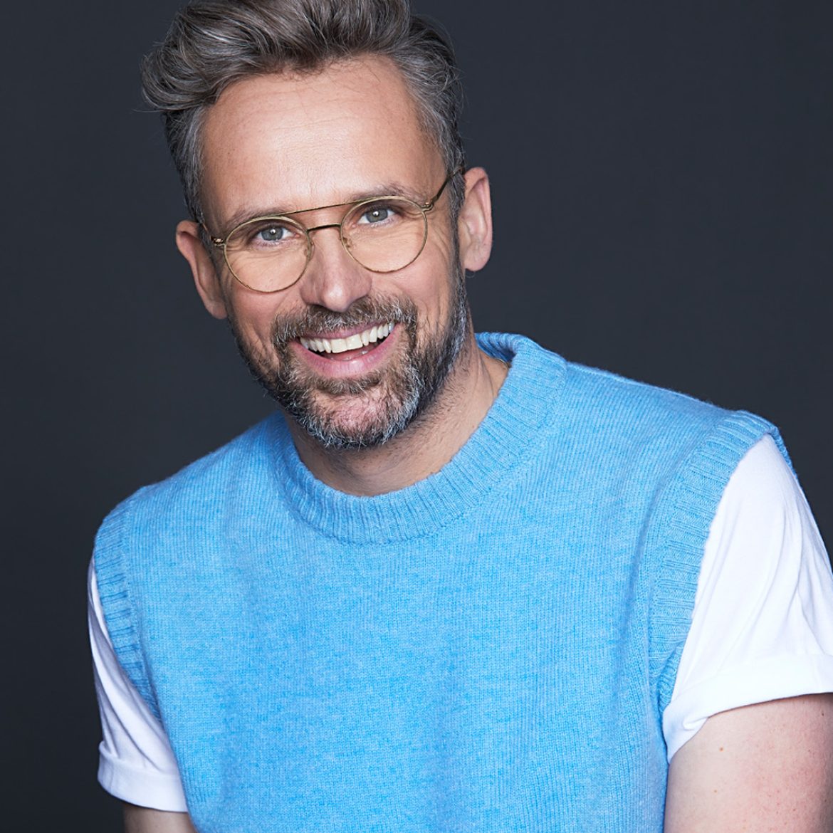 Lachende man met bril en wit shirt en hemelsblauwe spencer acteur Patrick Martins