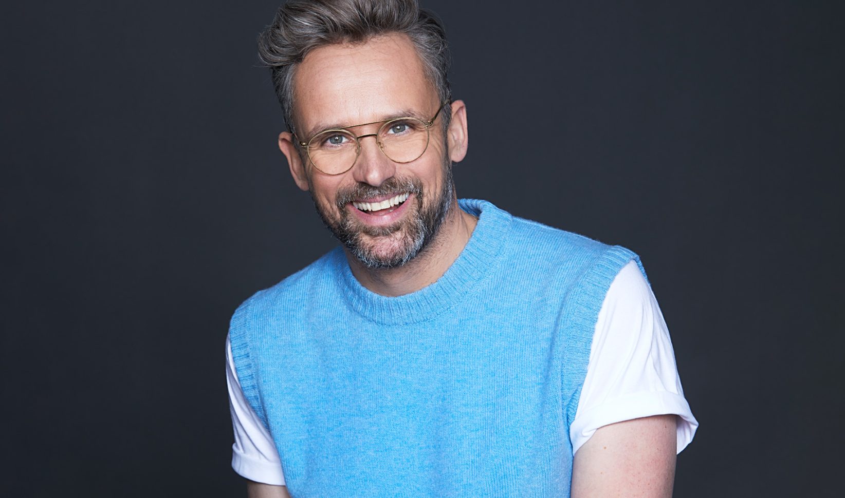 Lachende man met bril en wit shirt en hemelsblauwe spencer acteur Patrick Martins