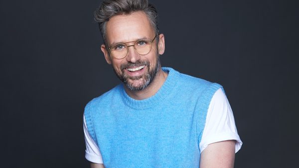 Lachende man met bril en wit shirt en hemelsblauwe spencer acteur Patrick Martins
