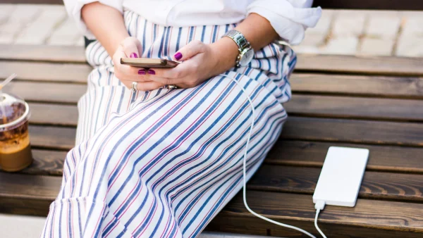 Een mevrouw laadt haar telefoon op met een powerbank op een bankje