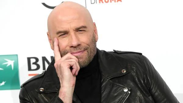 John Travolta met een zwart leren jack aan en hij leunt op zijn hand