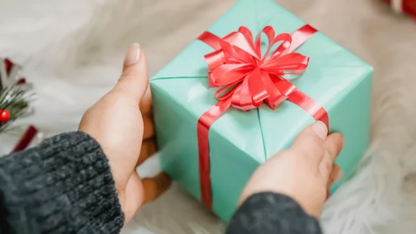 Vrouw zet cadeau neer in blauw inpakpapier met rode strik - We geven cadeautips onder de 20 euro