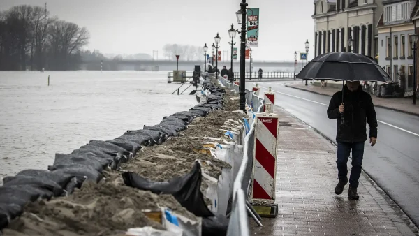 Een man met een paraplu loopt langs de kade in Deventer, die versterkt is met zandzakken