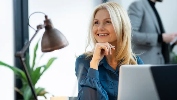 Een vrouw zit achter haar laptop en lacht naar iets buiten beeld