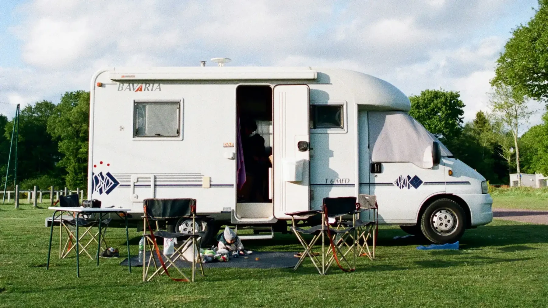 Een camper met een open deur en campingstoelen ervoor, ter illustratie