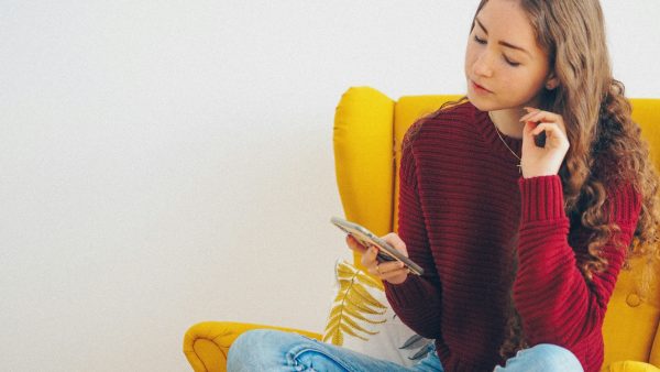 Jonge vrouw zit op gele stoel met telefoon in haar hand