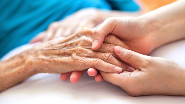 Vrouw houdt de hand van een oudere vrouw vast, ter illustratie van een hospice