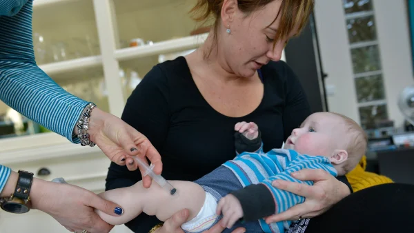 Vrouw houdt baby vast die een prik krijgt