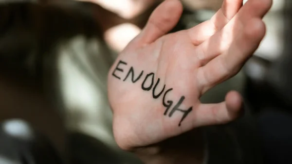 Hand met 'ENOUGH' erop geschreven, ter illustratie van seksueel geweld