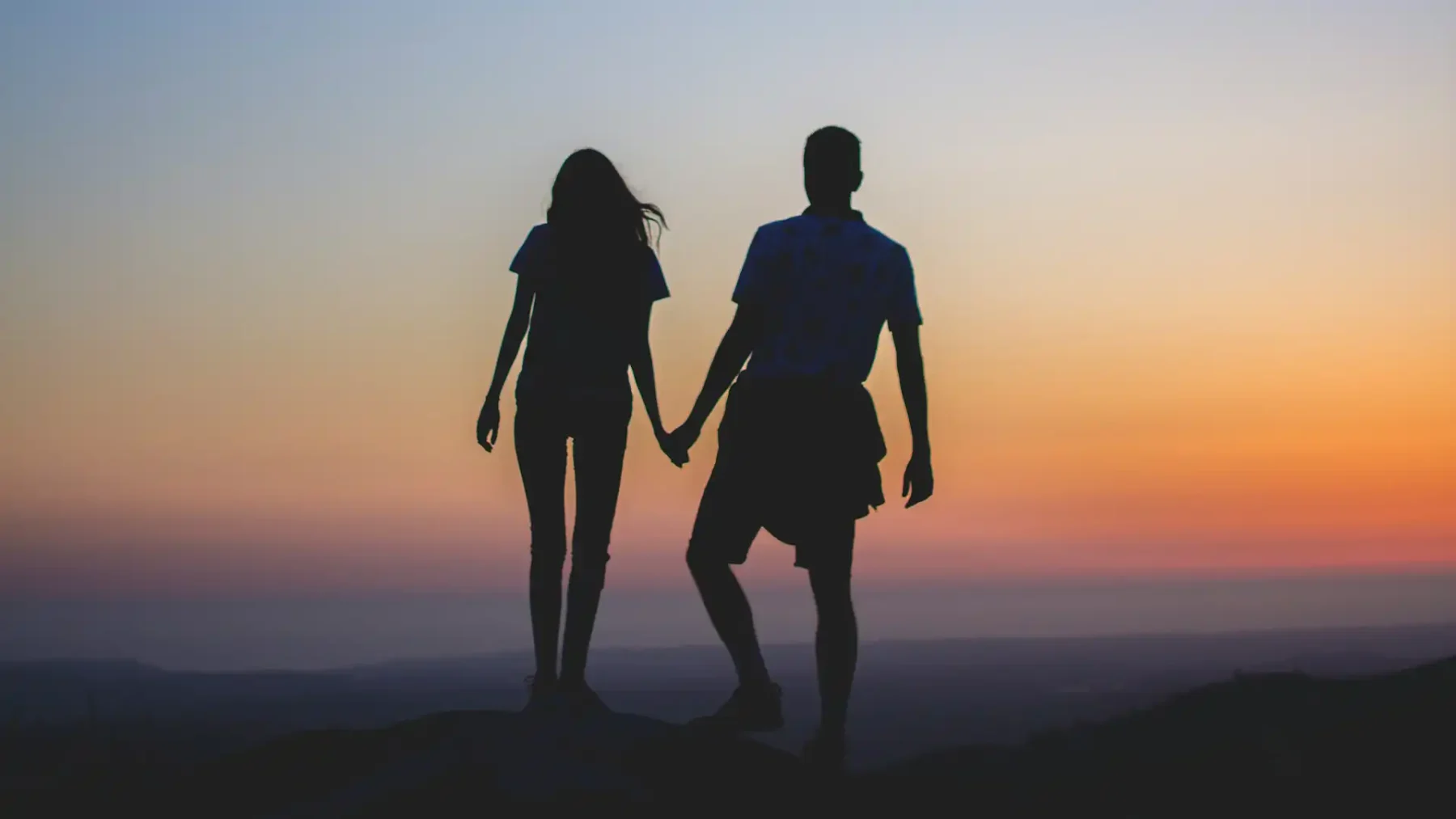 Een vrouw en een man kijken vanaf een bergtop naar de zonsondergang