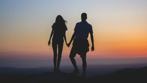 Een vrouw en een man kijken vanaf een bergtop naar de zonsondergang
