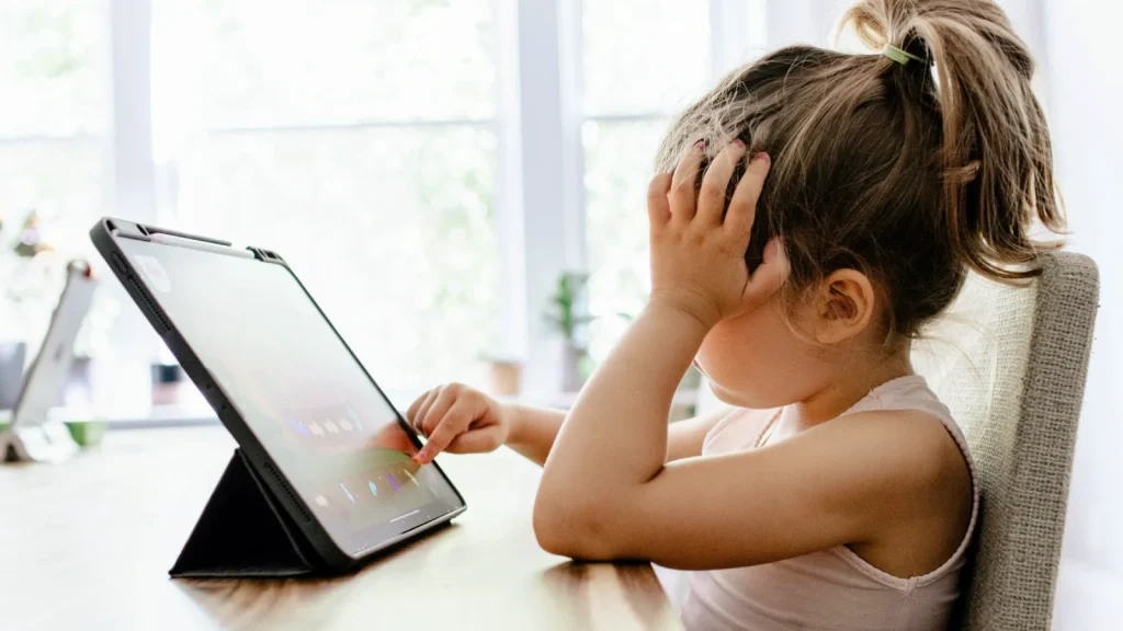 Jong meisje zit aan tafel en kijkt naar scherm op tablet