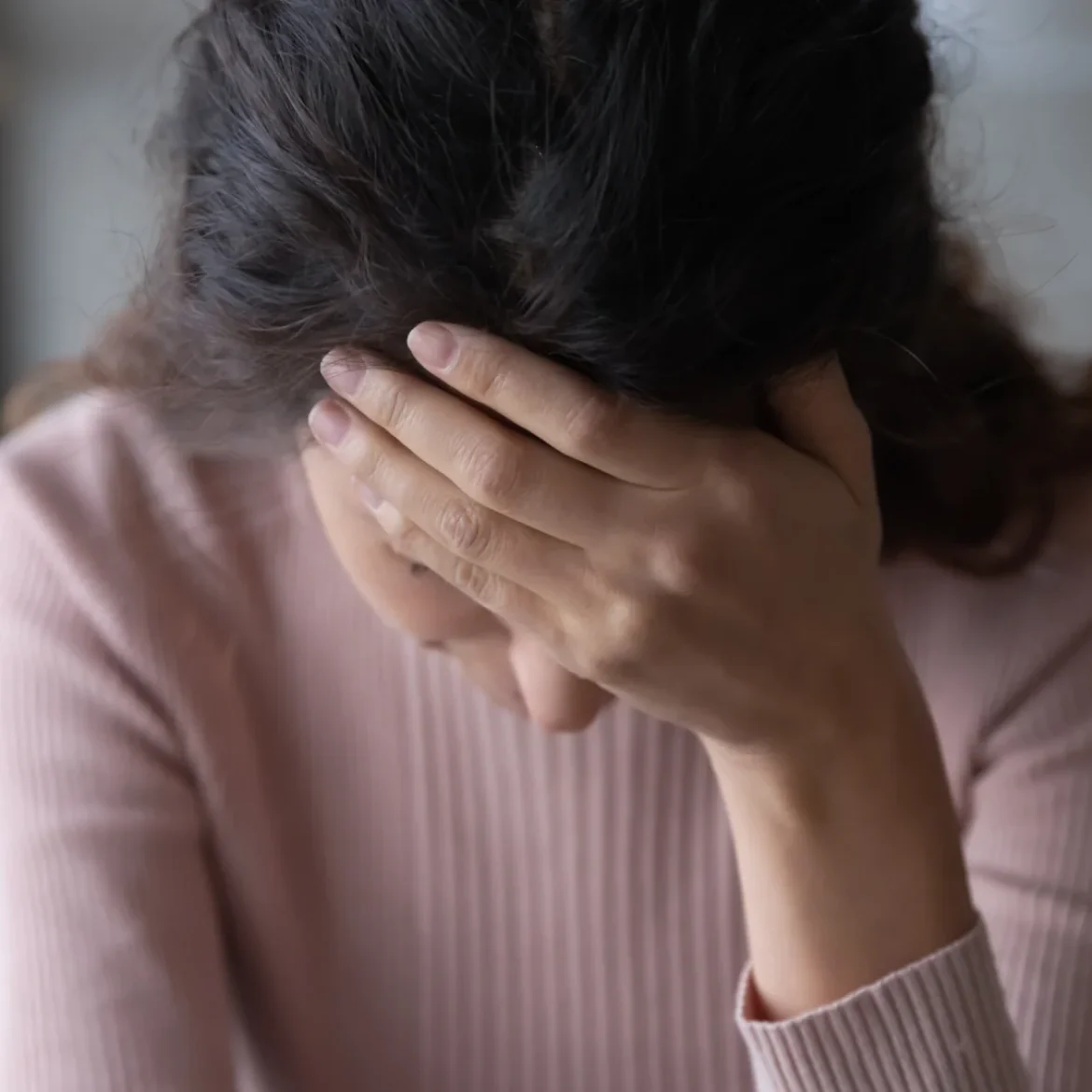 Vrouw met een roze trui zit verdrietig op de bank