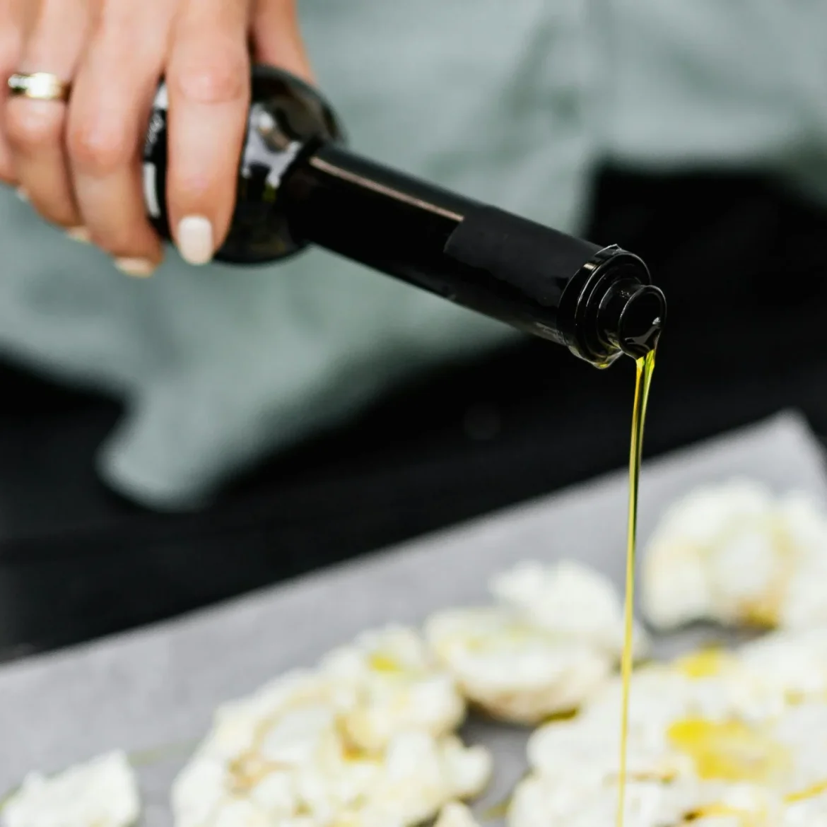 Vrouw giet olijfolie over bloemkool op bakplaat