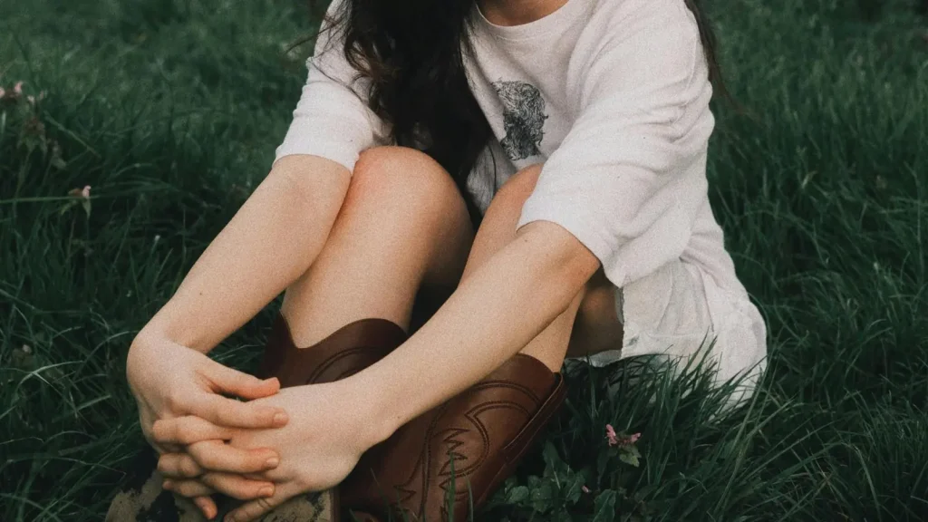 Vrouw houdt haar knieën vast en zit in een veld