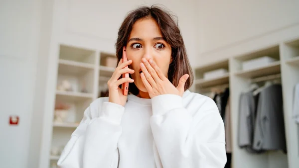 Vrouw telefoneert met een geschokte blik, na het zien van zweepjes in woonkamer van haar date