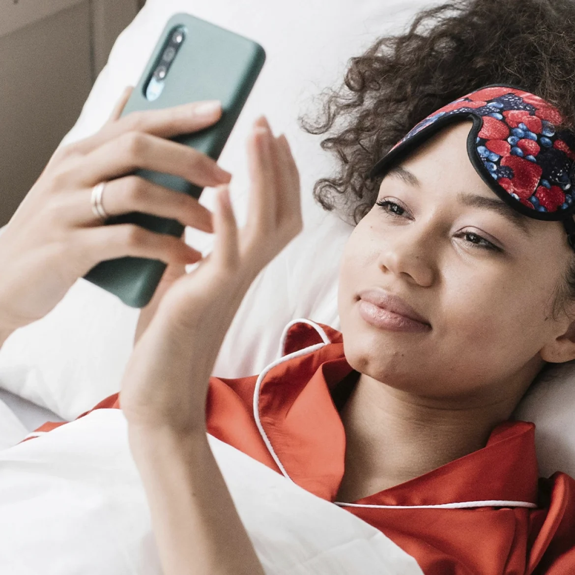 Vrouw met bruin haar en rood gelakte nagels kijkt op haar telefoon