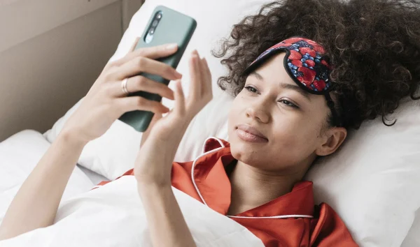 Vrouw met bruin haar en rood gelakte nagels kijkt op haar telefoon