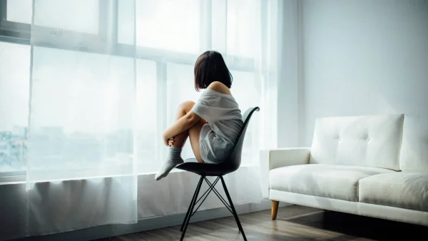 Vrouw kijkt uit het raam op stoel | Menstruatie