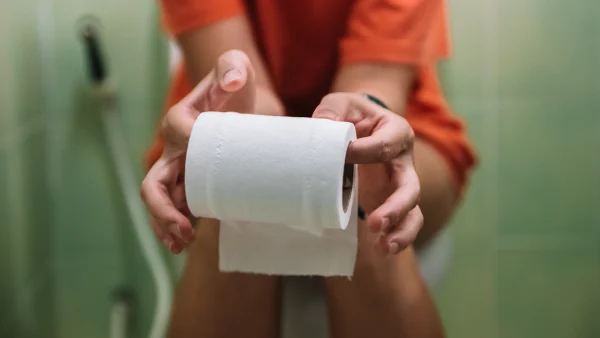 Vrouw zit aan de dunne op toilet met een rol wc-papier in haar handen