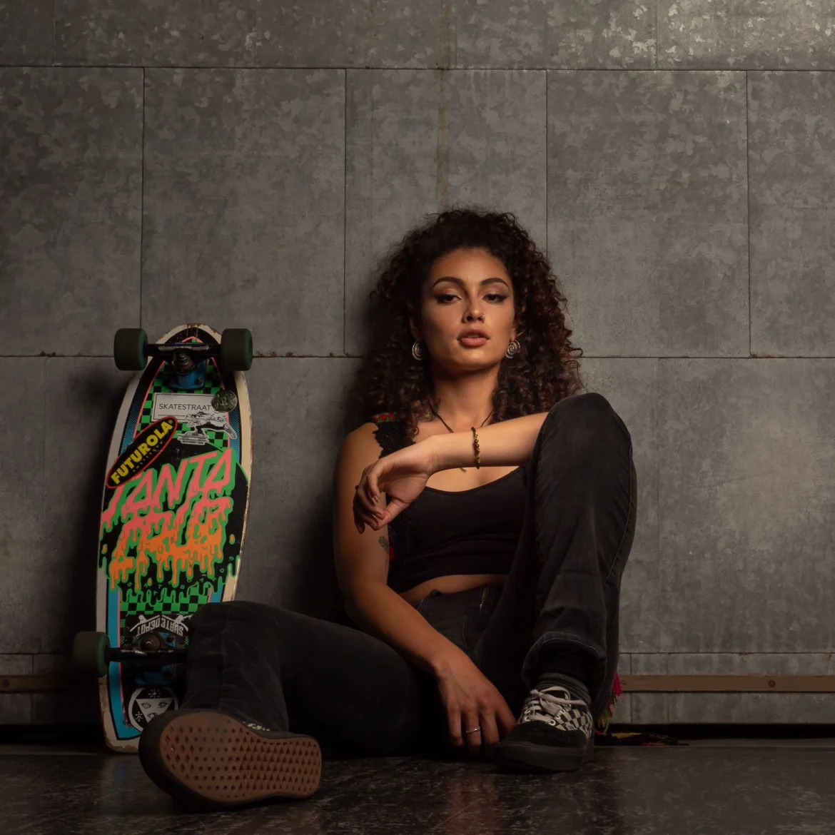 Vrouw zit naast skateboard tegen donkere achtergrond - Joël skatet van Nederland naar Portugal