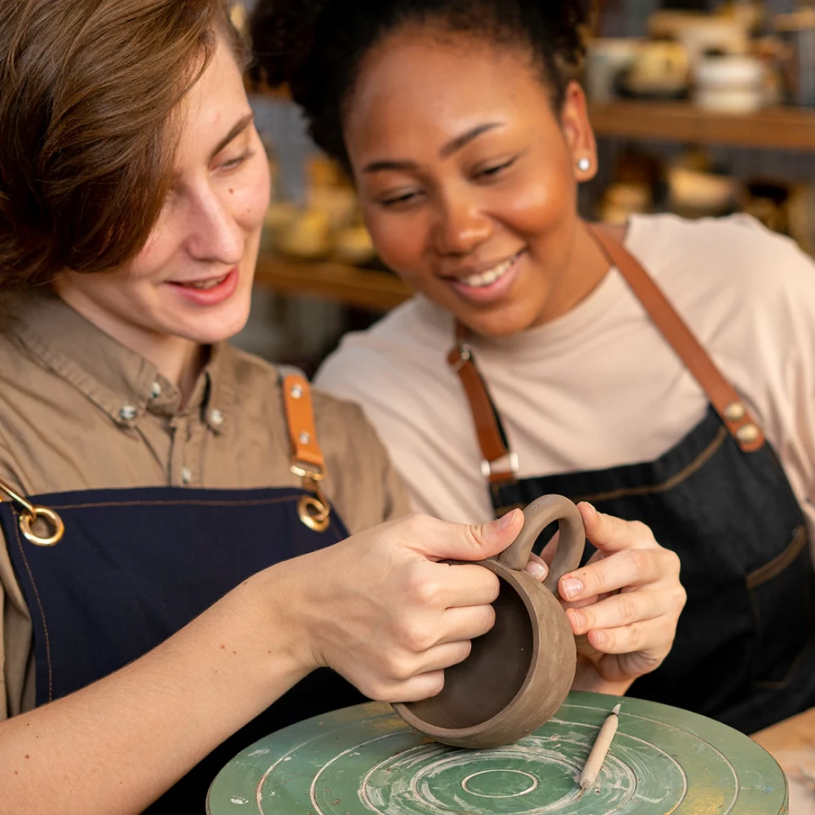 Twee vrouwen doen mee aan een workshop keramiek en zitten aan tafel te pottenbakken