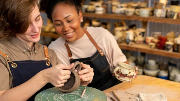 Twee vrouwen doen mee aan een workshop keramiek en zitten aan tafel te pottenbakken