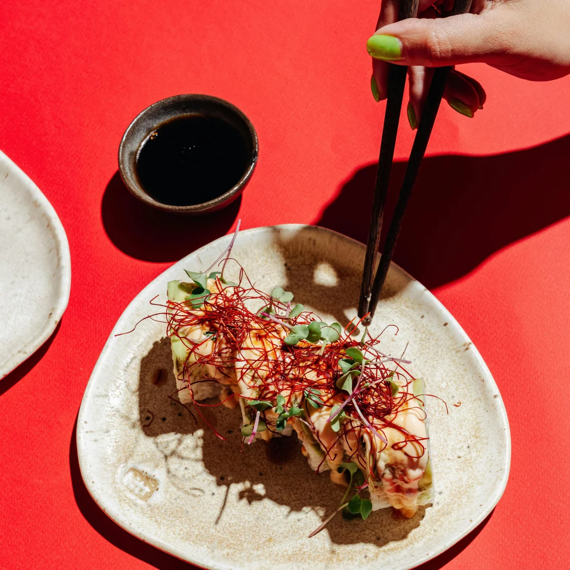 Vrouwenhand houdt stokjes vast en sushi op een rode achtergrond