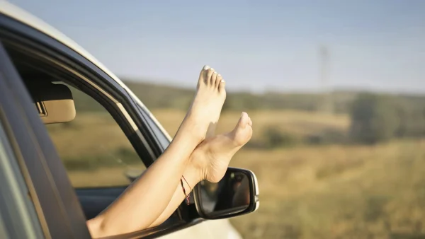 Blote benen uit een autoraam voor verkoeling in de zomer airco