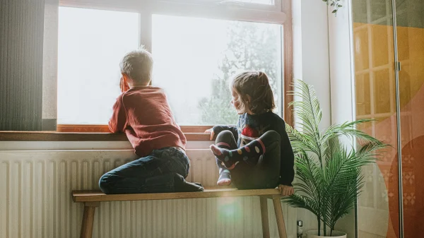 Twee kinderen in armoede zitten voor het raam tijdens de zomervakantie