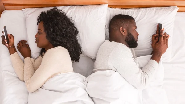Koppel in bed met ruggen naar elkaar toe en telefoon in hand. Voor een stuk over wat je moet doen als je iemand betrapt op liegen en wat de beste reactie is