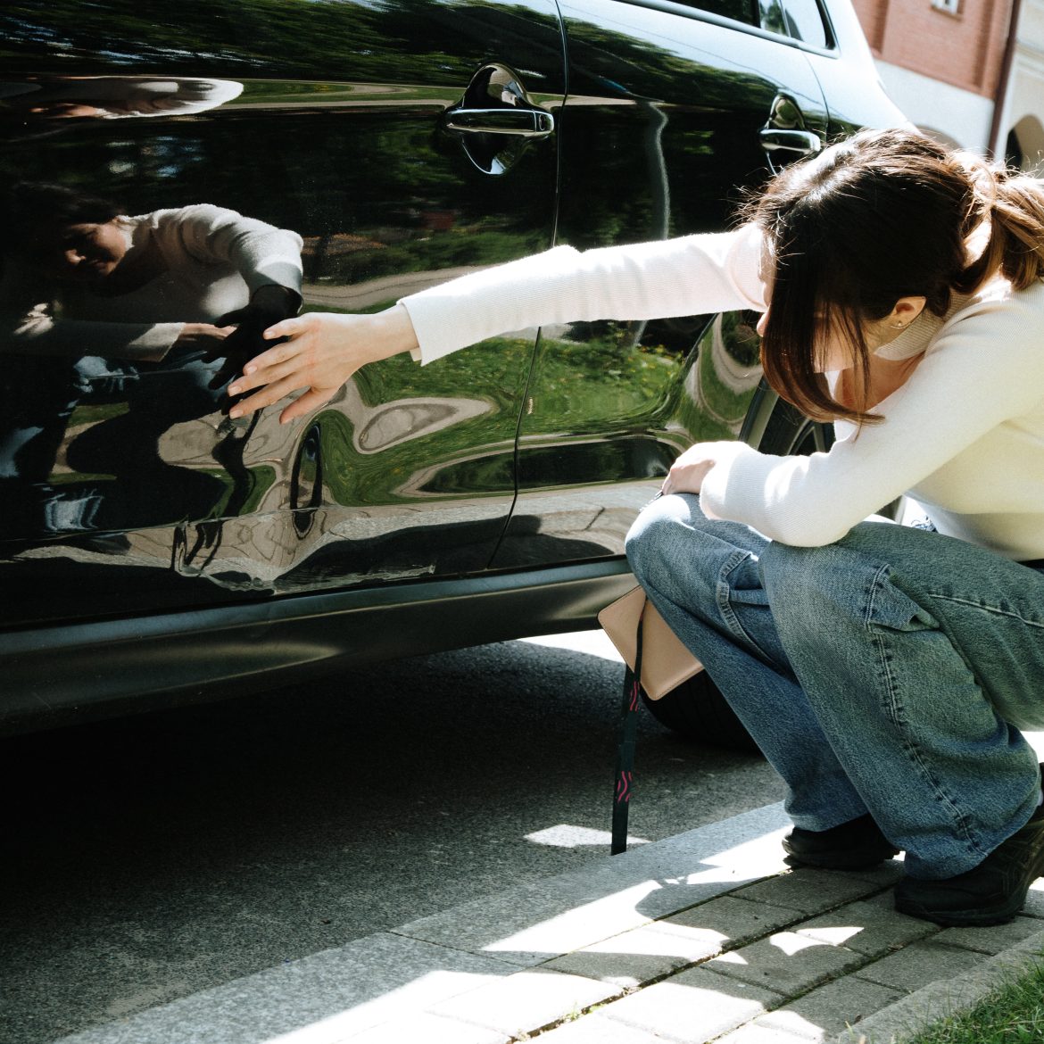 Vrouw zit voor een zwarte auto en bekijkt de autoschade
